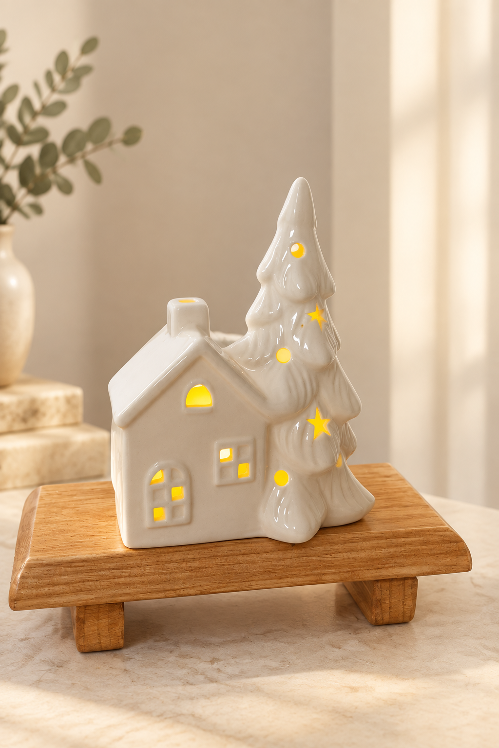 Casita y árbol de cerámica iluminados sobre base de madera, con luz cálida y fondo neutro
